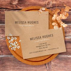 two business cards sitting on top of a wooden plate with dried flowers in the middle