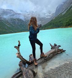 a woman standing on top of a tree branch next to a blue body of water