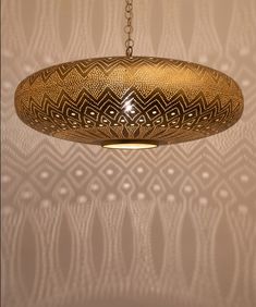 a light fixture hanging from a chain in front of a wall with intricate designs on it