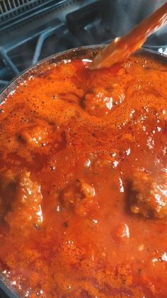 someone is stirring meatballs in a sauce on top of an open stove burner