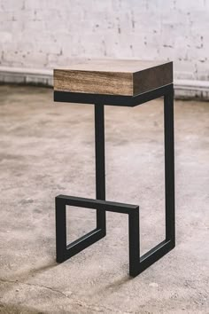 a wooden and metal stool sitting on top of a cement floor next to a brick wall