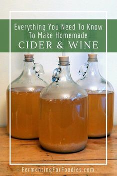 three glass bottles filled with cider and wine sitting on top of a wooden table