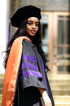 a woman wearing a graduation cap and gown standing in front of stairs with her hand on her hip