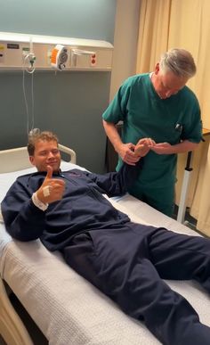 a man laying on top of a hospital bed next to an older man in scrubs