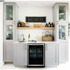 a kitchen with white cabinets and open shelving above the sink is filled with beverages