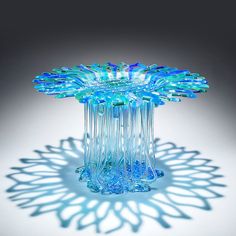 a blue glass vase sitting on top of a white table next to a shadow cast wall