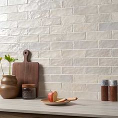 a white brick wall behind a counter with some fruit on it and a cutting board