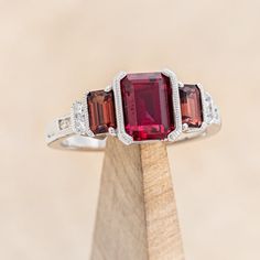 three stone ring with diamond accents on wooden stand in front of beige background, closeup