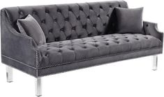 a gray velvet couch with silver legs and studded trimmings on the arms