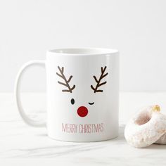 a white coffee mug with reindeer antlers on it and a donut next to it