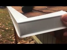 a hand holding a piece of wood on top of a wooden table in front of a house