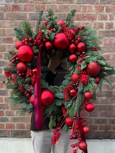 a man holding a wreath with red ornaments