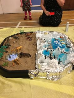 a woman sitting on the floor next to a cake with animals and sand in it