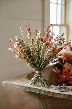 dried flowers in a vase sitting on a stone counter top next to an open window