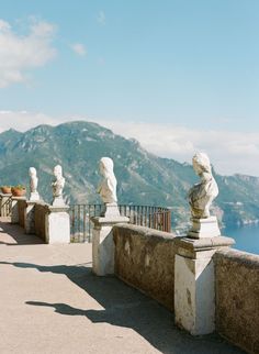 some statues are on the side of a building near water and mountains in the background