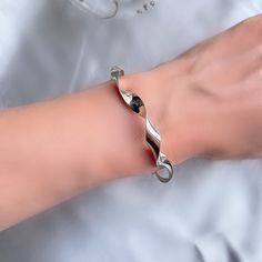 Our new unique curly bangle has a unique twist boasting a mesmerising high shine silver with kinks in its curve, like a skip in your step.  Diameter: 61 x 52 mm Top width 7 mm Weight approximately 22 grams Sterling Silver Bracelet With A Modern Twist, Silver Bracelet With Polished Finish And Modern Twist, Silver Bracelets With Polished Finish And Modern Twist, Silver Bracelets With A Modern Twist, Elegant Twisted Jewelry With Polished Finish, White Gold Bracelet With A Modern Twist For Gifts, Modern Twist White Gold Bracelet As Gift, Silver Bracelet With A Modern Twist, Twisted Polished Jewelry As A Gift