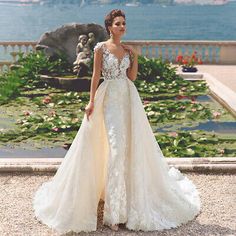 a woman standing in front of a lake wearing a wedding dress with flowers on it