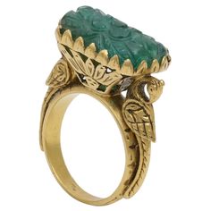 A Beautifully hand Carved Zambian Emerald set in a hand made 22K Gold Ring. The ring has intricate gold work and right below the stone are 2 magnificent peacocks holding the stone. The carved stone is inspired from the Mughal times when the Mughal rulers loved carvings on Gemstone. The national bird of India is a peacock which gave us inspiration to delicately make that on Gold. All around the stone is really intricate work done on the cocktail ring by our highly trained artisans who took long t Luxury Traditional Carved Rings, Antique Yellow Gold Emerald Ring, Antique Emerald Ring In Yellow Gold, Luxury Carved Rings, Luxury Green Intaglio Rings, Antique Intaglio Ceremonial Jewelry, Antique Intaglio Jewelry For Ceremonial Occasions, Art Deco Carved Round Jewelry, Antique Ceremonial Intaglio Jewelry