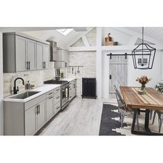 a kitchen with white walls and wooden flooring next to a dining table in front of an oven