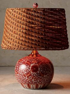 a red and white vase with a brown lamp shade on it's side, sitting on a table