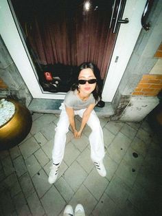 a woman sitting on the ground in front of a door with sunglasses on her face