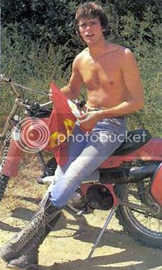 a shirtless man sitting on top of a red dirt bike with his legs crossed