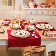 the table is set for christmas dinner with red and white dishes, silverware, and other holiday decorations