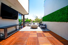 an outdoor living area with wood flooring and television mounted to the side of a building