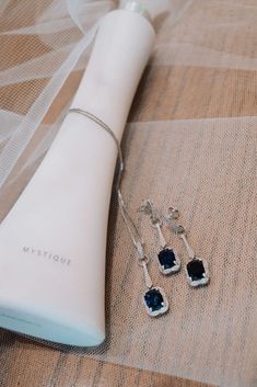 two pairs of earrings sitting on top of a bed next to a white vase and veil