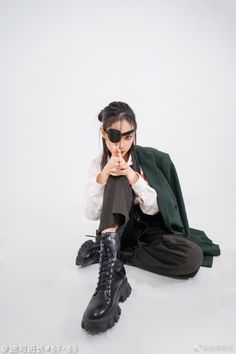 a young woman sitting on the ground wearing black boots and a green blazer jacket