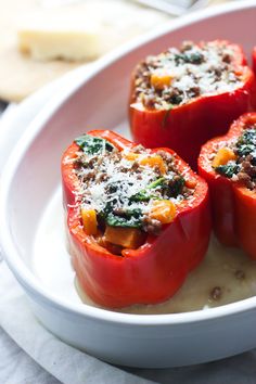 three stuffed peppers on a white plate with lettuce and tomatoes in the background