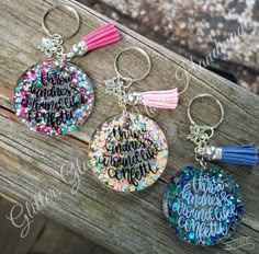 three key chains with words on them sitting on a wooden bench, one has a tassel and the other has a tassel