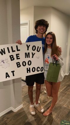 two people standing next to each other holding a sign that says will you be my boo at hoco?