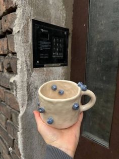 a hand holding a coffee cup with blueberries on it in front of a brick wall