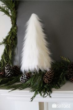 a white christmas tree sitting on top of a mantel covered in pine cones and fake fur