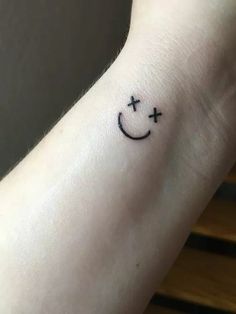 a smiley face tattoo on the wrist with two crosses in it's middle and one cross at the top