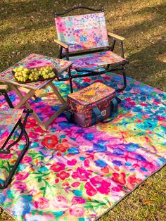 two lawn chairs sitting on top of a colorful blanket next to a picnic table filled with fruit