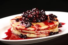 a stack of pancakes covered in blueberries and syrup on top of a white plate