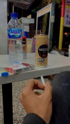 a person sitting at a table writing on a piece of paper next to a bottle of water