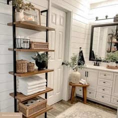 a bathroom with white walls and wooden shelves filled with towels, plants and other items