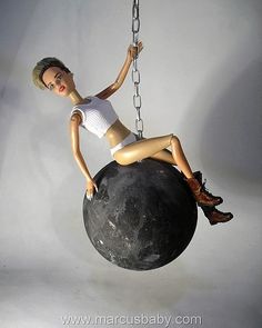 a doll sitting on top of a black ball suspended from a chain with chains around it