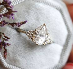 a person holding a ring on top of a white cloth with purple flowers in the background