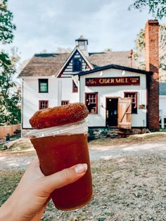 a person holding up a drink in front of a white building with a red roof