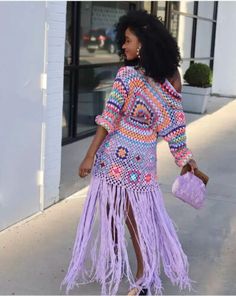 a woman walking down the street wearing a purple dress with fringes and a pink purse