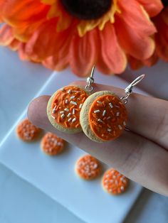 a person is holding two orange cookies in front of a flower and some small white sprinkles