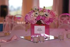 a table with pink and white flowers in a square vase on top of the table