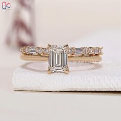 an emerald cut diamond engagement ring on top of a white napkin with a gold band