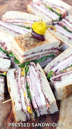 a pile of sandwiches sitting on top of a wooden cutting board