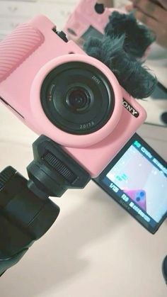 a pink camera sitting on top of a tripod next to a cell phone holder