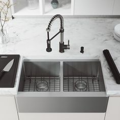 two stainless steel sinks in a white kitchen with marble counter tops and black utensils